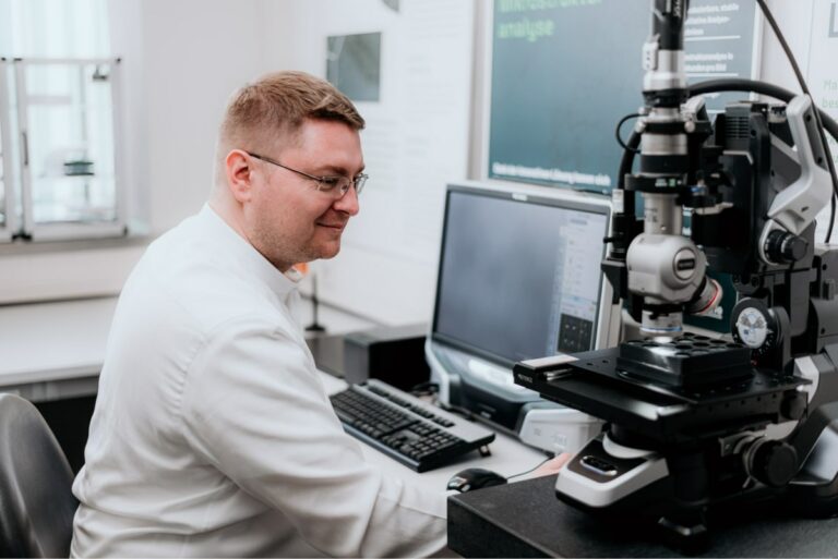 Man sitting next to microscope analyzing microstrucure images.